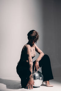 Rear view of woman holding ball while standing against wall at home