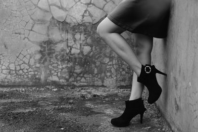 Low section of woman wearing high heels while leaning on wall