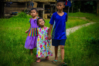 Full length of siblings walking on pathway amidst grassy field