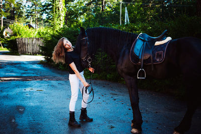 Portrait of young woman standing with horse against trees