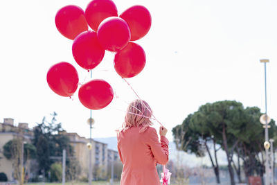 Rear view of woman standing with pink balloons against sky