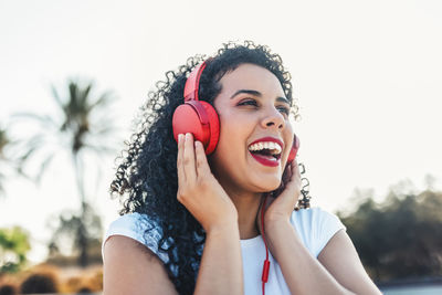 Cheerful woman listening to music through wired headphones at skateboard park