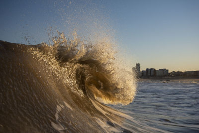 Waves splashing in sea against clear sky