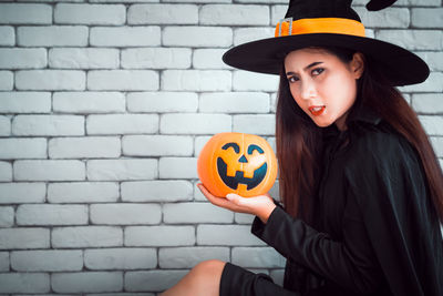 Young woman holding pumpkin against stone wall during halloween