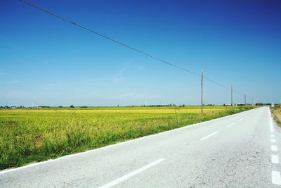 Road by field against clear blue sky