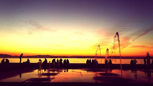 Silhouette people on beach against sky during sunset