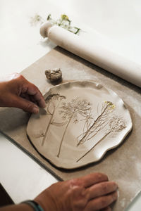 Hands making clay handmade ceramic plates, rolled clay on the table with plants and flowers. top