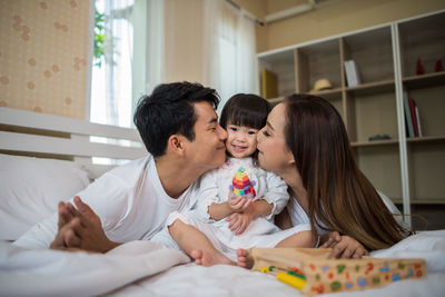 Parents kissing daughter on cheek at home