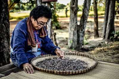 Woman wearing hat sorting rice against trees