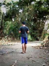 Rear view of boy standing on footpath against trees