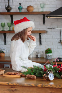 Kid sitting in christmas decorated cozy kitchen and wearing red santa claus hat