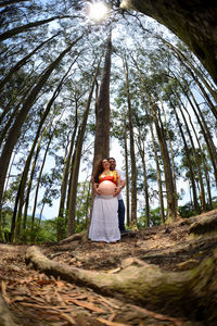 Pregnant woman and his husband standing by tree trunk in eucaliptus forest