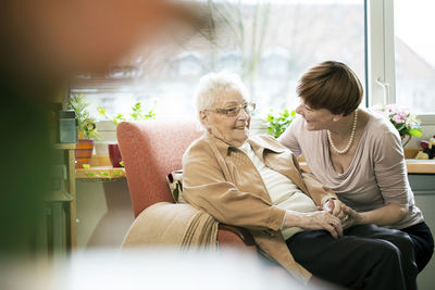 Adult daughter talking to her mother with alzheimer's disease in her room at retirement home