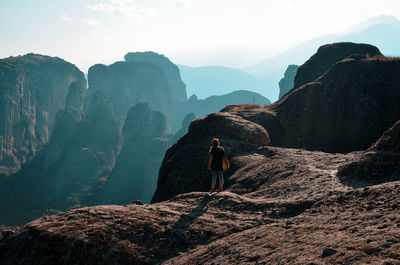 A beautiful view of a woman standing on a edge of a rock on a sunny day 