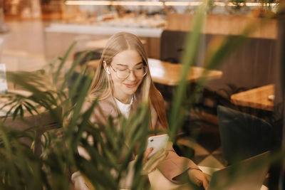 A millennial business woman works and studies online using a mobile phone and technology in a cafe