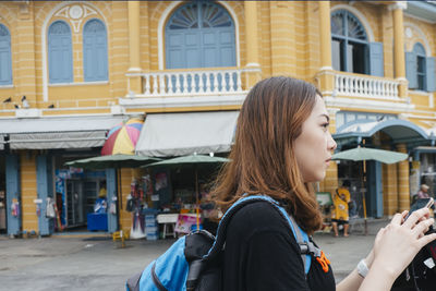 Side view of woman sanding against building outdoors