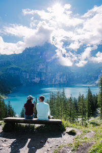 Rear view of men sitting on mountain against sky