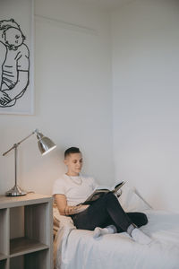 Young man using mobile phone while sitting on bed at home