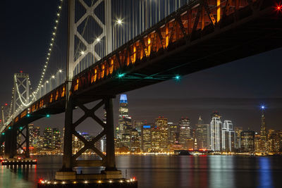 Illuminated bridge over river in city at night