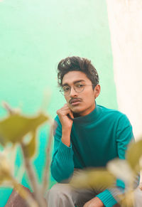 Portrait of young man sitting against wall