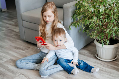 Girl with a baby brother sitting on the floor with a smartphone