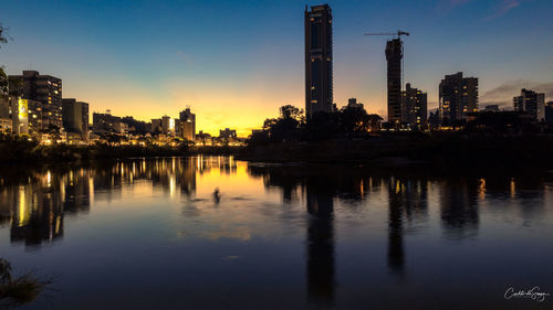 Scenic view of river by illuminated buildings against sky during sunset