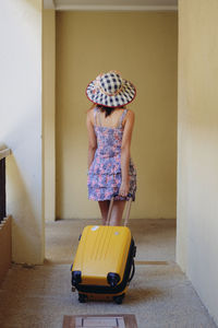 Rear view of young woman with wheeled luggage walking in corridor