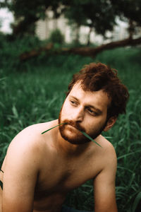 Shirtless young man looking away on field