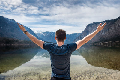 Rear view of man standing on mountain by lake