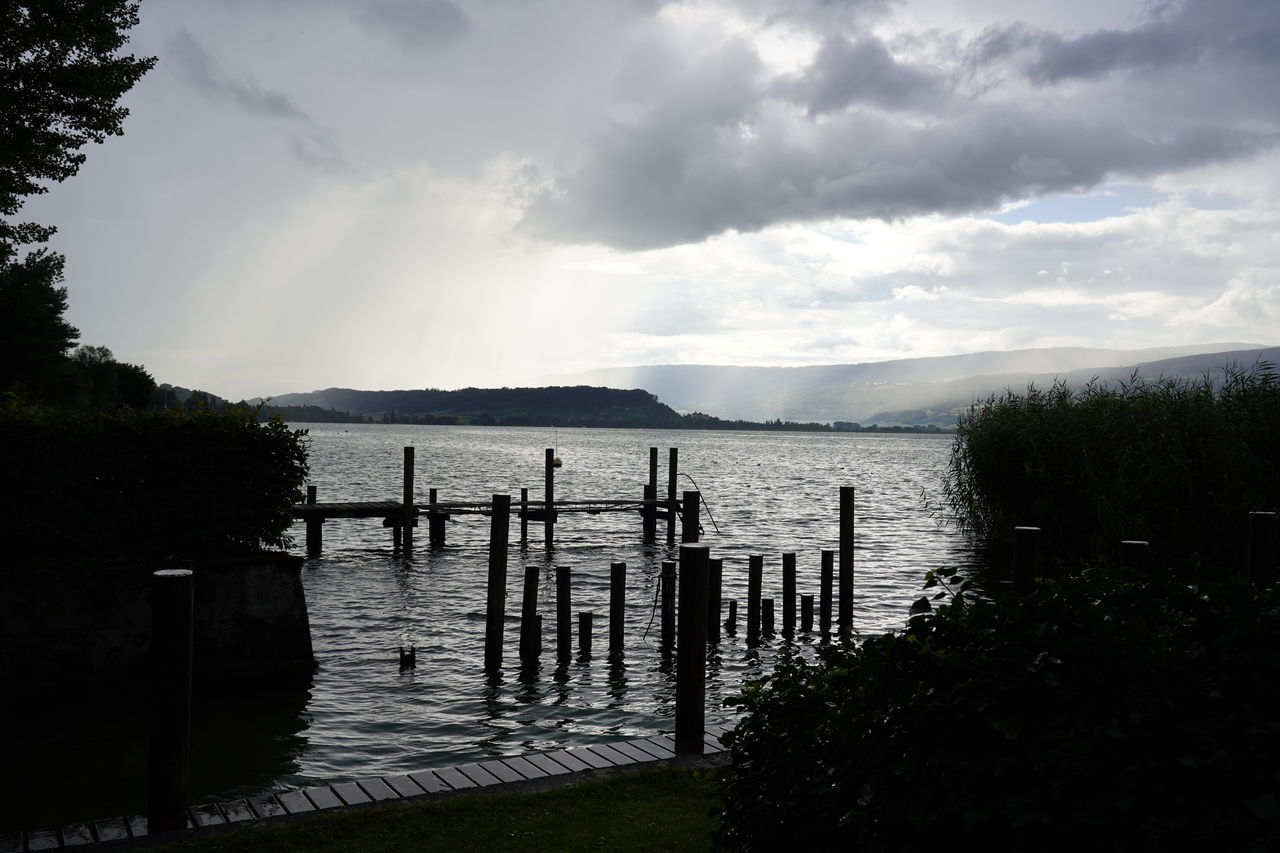 SILHOUETTE WOODEN POSTS IN LAKE AGAINST SKY