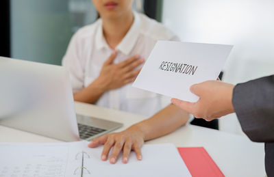 Cropped hand of business person giving resignation letter to colleague in office