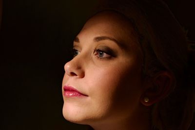 Close-up portrait of woman looking away against black background