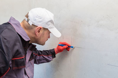 A man, an electrician marks out holes for sockets with a pencil, a tape measure