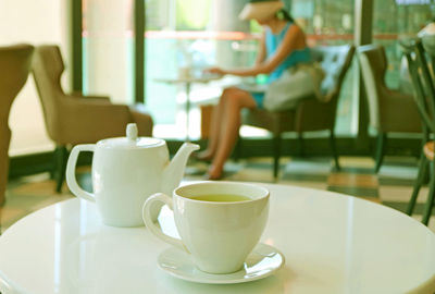 Close-up of tea cup on table with woman sitting in background at cafe