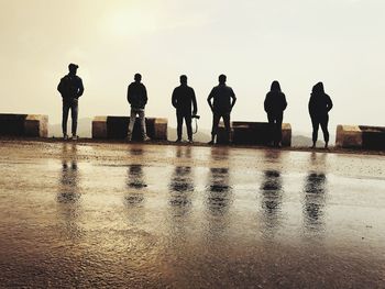 Rear view of people standing on wet mountain road against clear sky