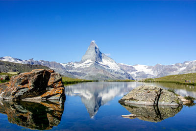 Scenic view of lake and mountains against clear blue sky