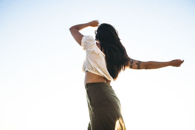 Young latina woman dancing by the ocean at golden hour in summertime