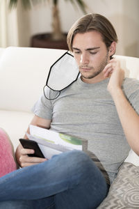 Young man using smart phone sitting on sofa at home