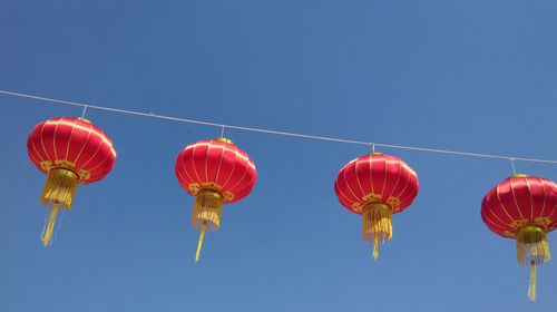 Low angle view of chinese lanterns hanging against clear blue sky