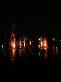 Illuminated city by river against sky at night