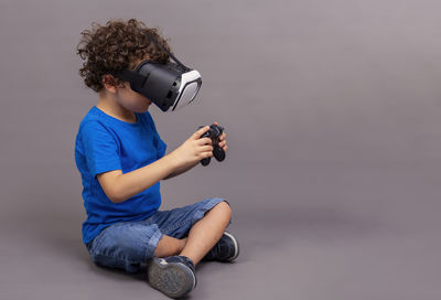 Caucasian boy sitting on the floor with virtual reality goggles and game controllers in his hands