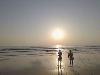 Silhouette people on beach against sky during sunset