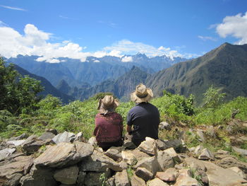 Rear view of people sitting on mountain against sky