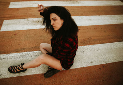 High angle view of young woman sitting on zebra crossing