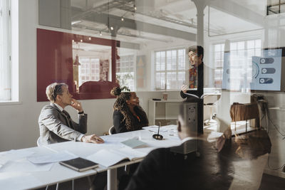 Business colleagues conducting meeting in board room at office seen through glass