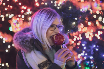 Young woman eating caramelized apple during christmas at night