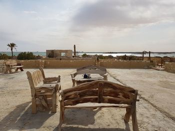 Empty chairs and table at beach against sky