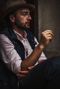 Young man wearing hat smoking cigarette in city