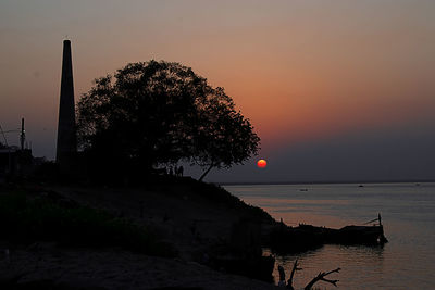 Silhouette tree by sea against sky during sunset
