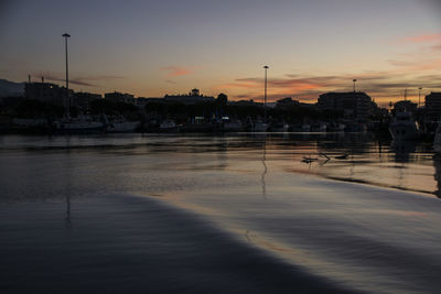 Silhouette buildings by river against sky during sunset